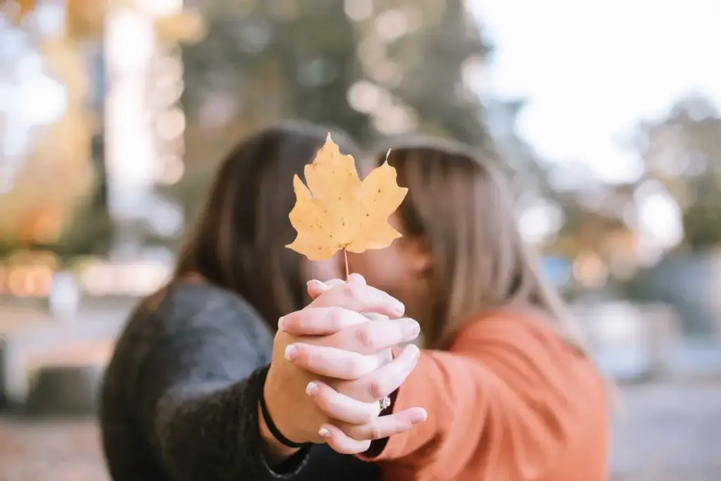 A Charlotte, NC couple kiss and hold a fall leaf during their engagement photography session at Marshall Park.