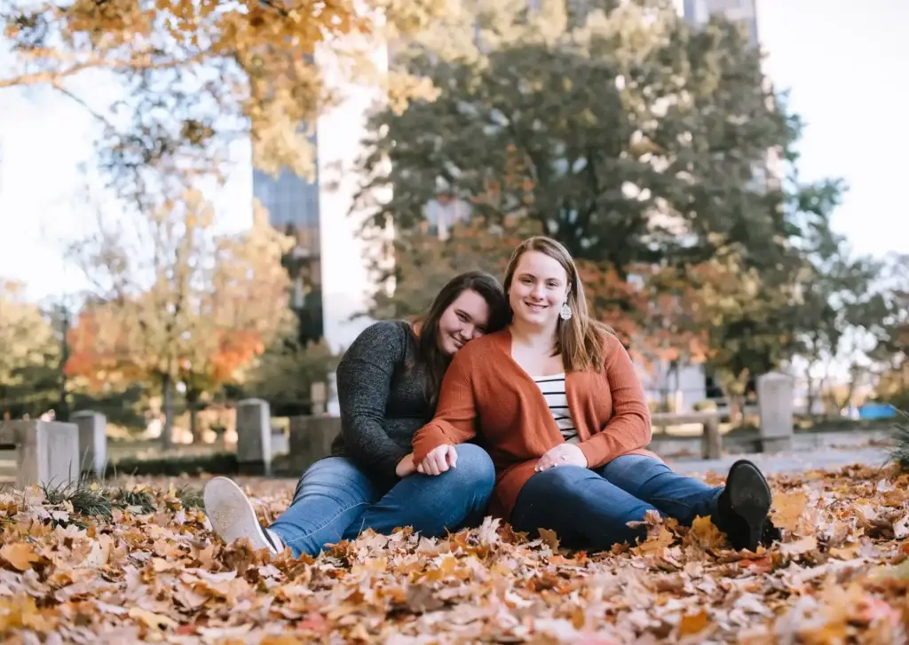 A couple sit on a blanket and smile while being photographed during their fall engagement photography session at Marshall Park in Charlotte, NC